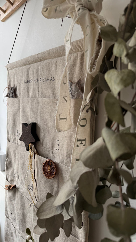 Fabric advent calendar with decorative elements hanging on a wall.