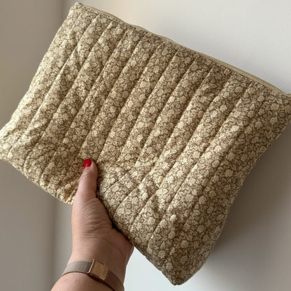Hand holding a textured green floral, quilted washbag against a neutral background