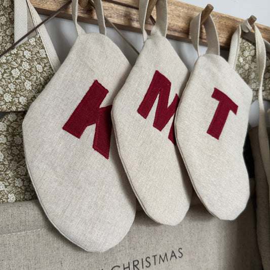 Three Mini linen stockings with red initials hanging from a wooden rail