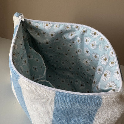 A zippered storage pouch or bag with a light blue and white striped exterior and a light blue interior printed with white daisies, shown on a neutral tabletop.