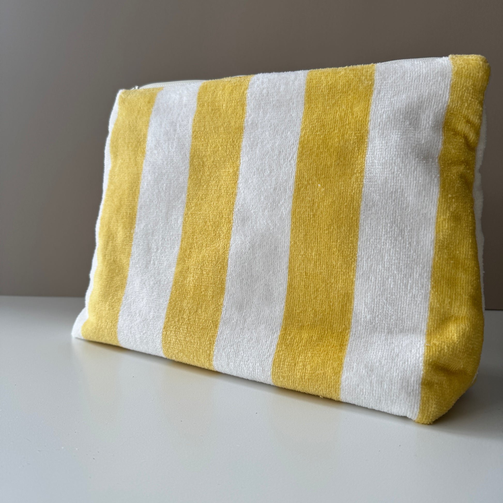A rectangular fabric pouch with vertical yellow and white stripes, photographed on a light surface against a plain neutral background.