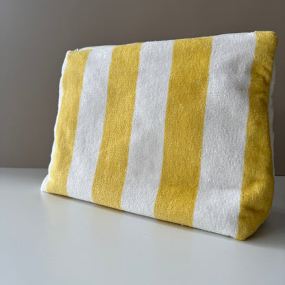 A rectangular fabric pouch with vertical yellow and white stripes, photographed on a light surface against a plain neutral background.