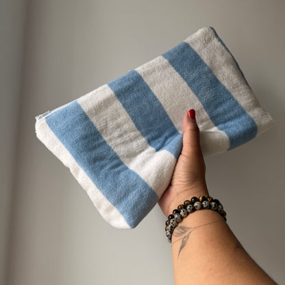 A hand holding a cosmetic pouch striped fabric, featuring alternating light blue and white stripes.