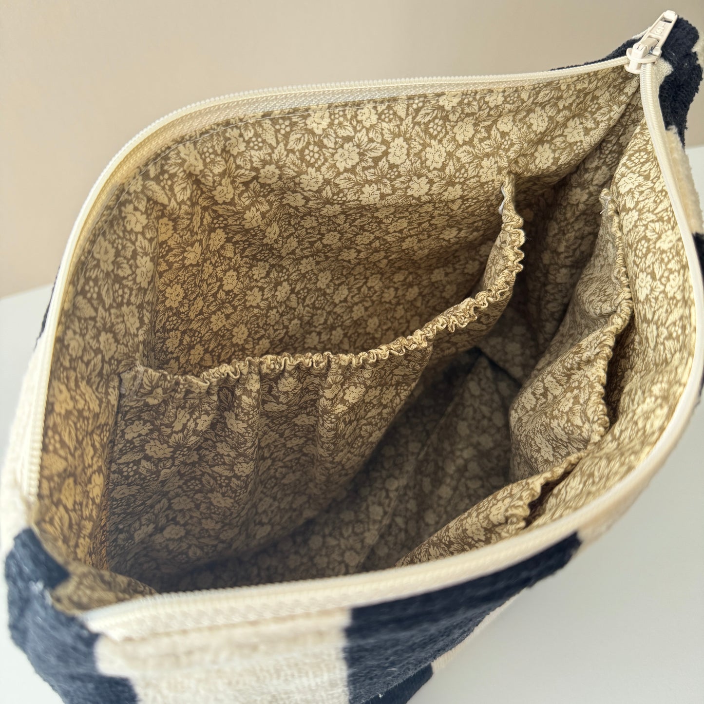 Inner lining of a cosmetic pouch with black and cream stripes. The lining is green and beige with floral details
